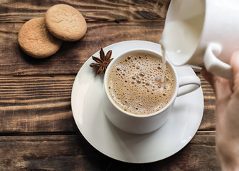 Hand holding cap of milk and pouring it to cap of coffee  on small plate with two small chocolate.   Flat Lay with no people