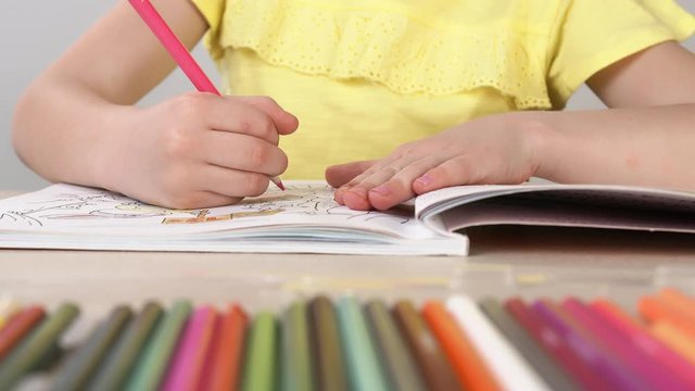 A girl paints a coloring book. Close-up of a little girl's hand holding a pencil and drawing.