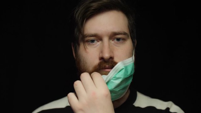 Bearded male takes off his protective mask with a sad look. This is the end. Hygiene concept. prevent the spread of germs and bacteria and avoid infection with the crown virus.