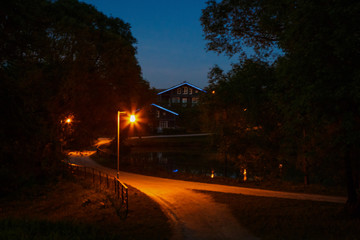 The road to the house at night, lit by a lantern. Yellow light of a street lamp in a Park on a road in a rural area