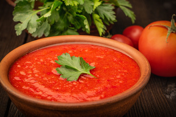 Bowl of tomato soup and fresh tomatoes with parsley on a wooden background