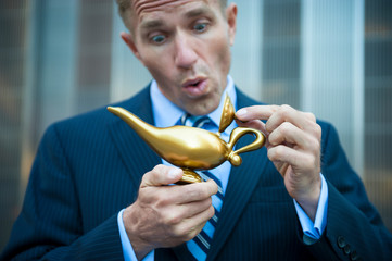 Businessman peeking in a golden magic lamp looking for the genie to come out and grant his three...