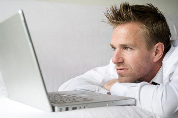 Guy in white shirt relaxing on white couch watching his computer screen