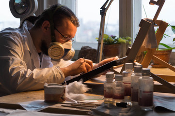 The master restorer in a white coat and respirator restores the icon, the restorer works in his...