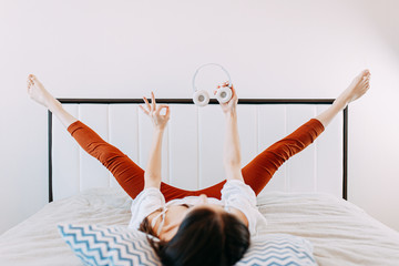 Naklejka premium Woman in bed while quarantine doing exercises in headphones, doing sports at home while self-isolation, home yoga, white bed and blue pillows.