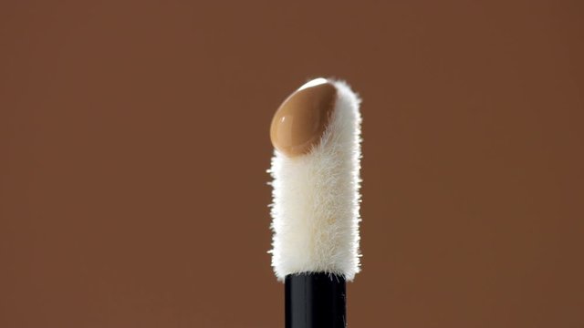 a clean white concealer stick and a drop of concealer pouring on it. Macro of concealer stick with product