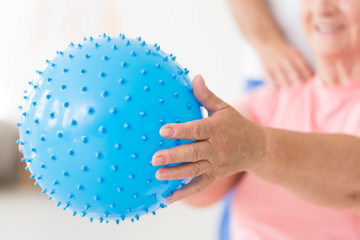 Close-up of a blue, bumpy exercise ball held by a senior woman