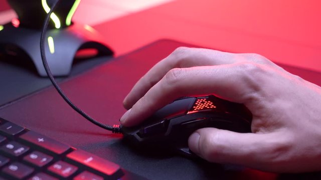 Gaming Device Mouse. A gamer is playing in a computer club. In the frame, the hand of a gamer and a gaming mouse. Red and violet colors. ESports competitions.

