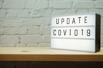 Update Covid-19 word in light box on wooden shelve and white brick wall
