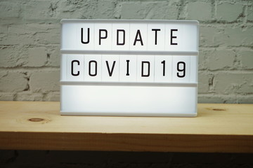 Update Covid-19 word in light box on wooden shelve and white brick wall