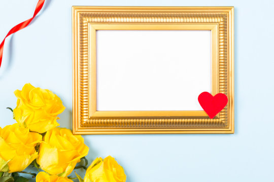 Close- up Golden frame empty blank picture and yellow roses on light blue background . Copy space free space for text. Holiday card concept. Mock up. Greeting. Mother's Day. St Valentine's Day. Love .