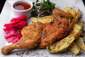 Half tobacco chicken with potatoes and sauce, on a white plate
