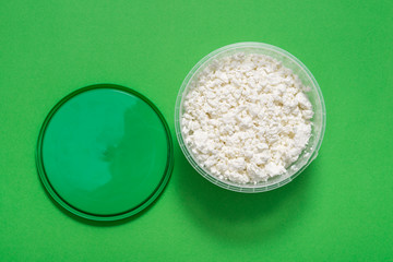 White cottage cheese in plastic jar on green background
