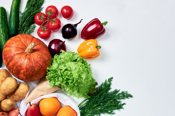 Groceries: pumpkin, potatoes, sprig of tomatoes, onions, red and yellow bell peppers, cucumbers, dill, oranges, red pears, lettuce on white background, packed on the left