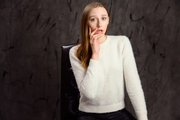 Studio portrait of a pretty caucasian blonde girl showing different emotions. A woman sits on a chair on a gray stylish background.