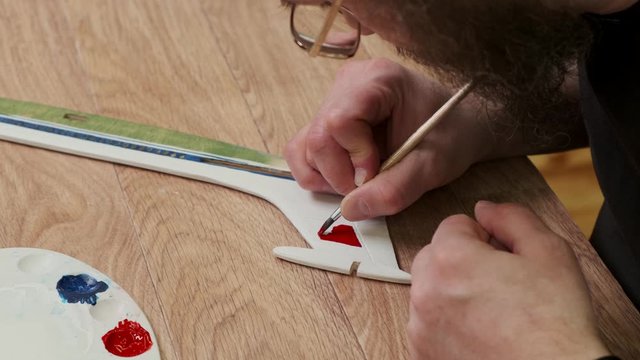 middle aged teacher draws on wooden tail of passenger airplane with red paint at table at Sunday school closeup slow motion