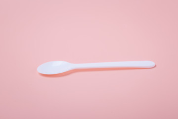 White plastic spoon on pink background
