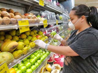 woman choosing green apples with mask and glove, protection against coronavirus.