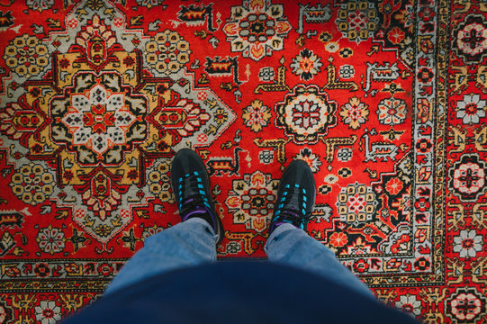 Man Stands On The Carpet And Takes A Photo Of His Feet. Fashionable Sneakers On Her Feet And Wears Jeans. Background. Photo Of Legs With Sneakers And Jeans, Top View, Standing On The Carpet.