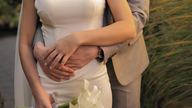 Wedding couple. The groom hugges the bride. Bride and groom embracing outdoors. Man and woman in love. Lovely groom and bride. Wedding day.   Bride holding her wedding bouquet of white callas.