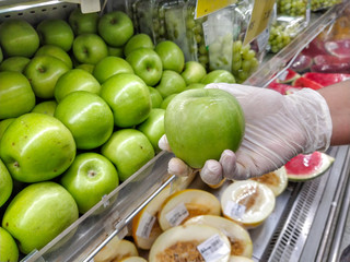 gloved hand holding a green apple, protection against coronavirus.