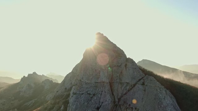 AERIAL mountain range in autumn sun beams and glare against the top at the foot of the mist
