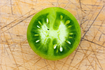 Naklejka na ściany i meble Green Tomato sliced in half, isolated on a cutting board background. Top down view into a juicy green tomato, seeds, flesh and juice.