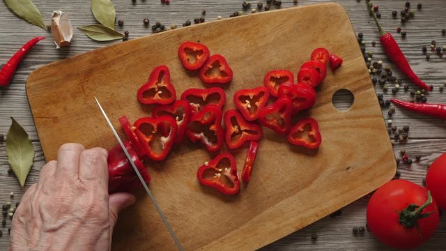 Using Knife To Cutting Ramiro Red Hot Pepper On Cutting Wooden Board. Top View. Close Up. Green Bay Leaf, Multi Color Peppercorns, Tomatoes And Bright Red Chili Pepper On Gray Wooden Background..