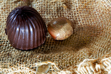 chocolate candies with nuts in the sun on a dark background of their burlap, close-up