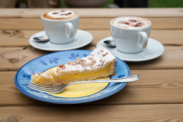 A piece of lemon cake and two cup of coffee on wooden table