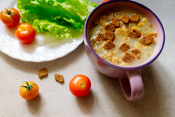 Soup with rye crackers, lettuce and fresh cherry tomatoes on a gray background
