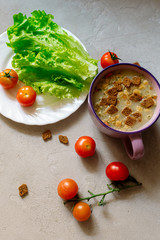 Soup with rye crackers, lettuce and fresh cherry tomatoes on a gray background
