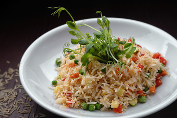 Rice with vegetables on a white plate, on a dark background
