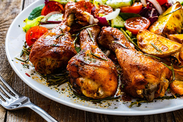 Barbecue chicken drumsticks with vegetables on wooden table