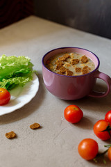 Soup with rye crackers, lettuce and fresh cherry tomatoes on a gray background
