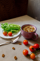 Soup with rye crackers, lettuce and fresh cherry tomatoes on a gray background
