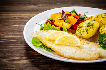 Fish dish - fried cod fillet with potatoes and vegetables on wooden table
