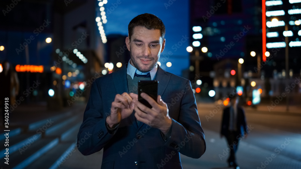 Wall mural portrait of caucasian businessman in a suit is using a smartphone on dark street in the evening. he 