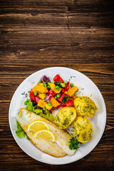 Fish dish - fried cod fillet with potatoes and vegetables on wooden table
