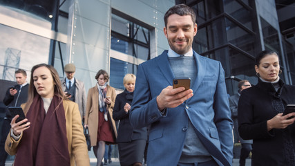 Office Managers and Businessmen are Walking in Front of a Modern Glass Office Building and Use Their Smartphones. People are Dressed Smartly and Look Successful. They are Occupied by Their Devices.