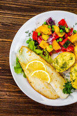 Fish dish - fried cod fillet with potatoes and vegetables on wooden table
