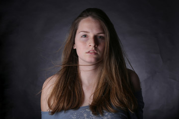 Studio portrait of young girl with light hair and freckles, with dark background.