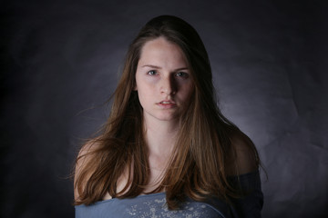 Studio portrait of young girl with light hair and freckles, with dark background.