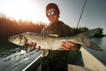 Happy fisherman holds trophy Asp fish standing in the boat