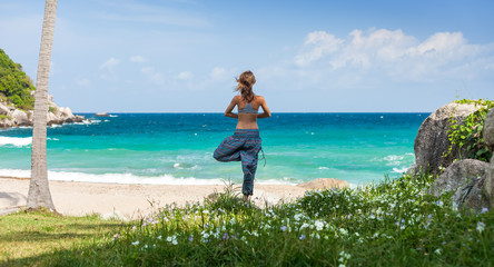 Young woman performs yoga exercises on a green lawn with sea on the background