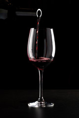 Red wine being poured into a glass and splashing over the side. Low key black background.