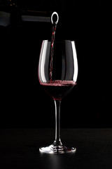 Red wine being poured into a glass and splashing over the side. Low key black background.