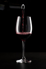 Red wine being poured into a glass and splashing over the side. Low key black background.