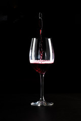 Red wine being poured into a glass and splashing over the side. Low key black background.
