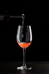 Rose wine pouring in a glass on black background
